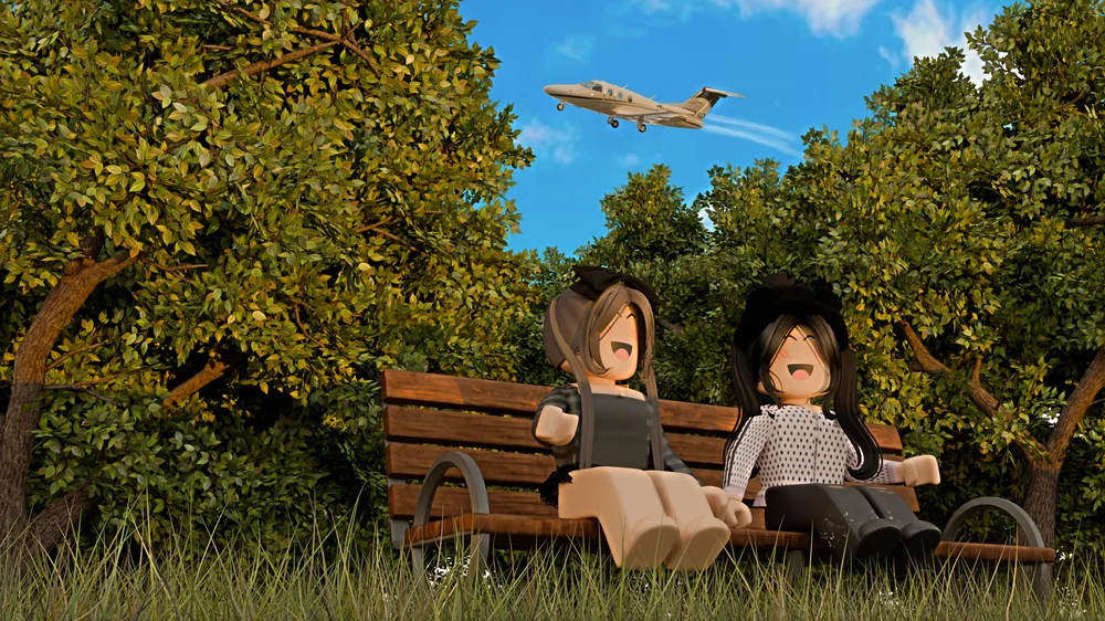 Two friends laughing on a wooden park bench in tall grass, framed by leafy trees, as a private jet flies low overhead against a blue sky.